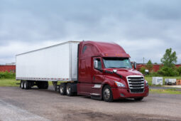 A red semi truck with its trailer parked on the side of the road.