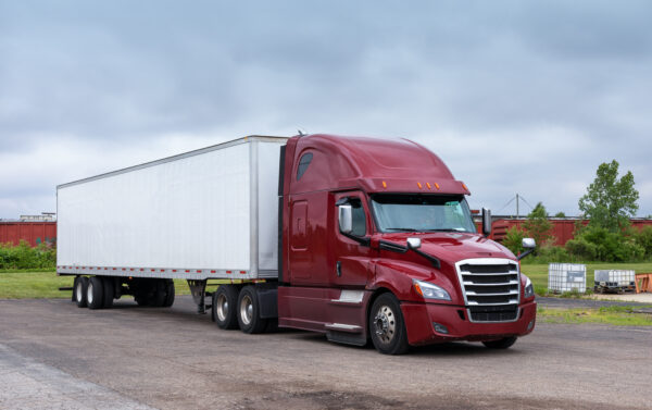 A red semi truck with its trailer parked on the side of the road.