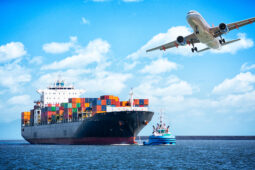 A large cargo ship with a plane flying over it.