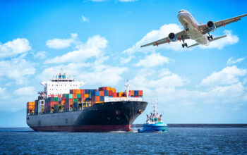 A large cargo ship with a plane flying over it.