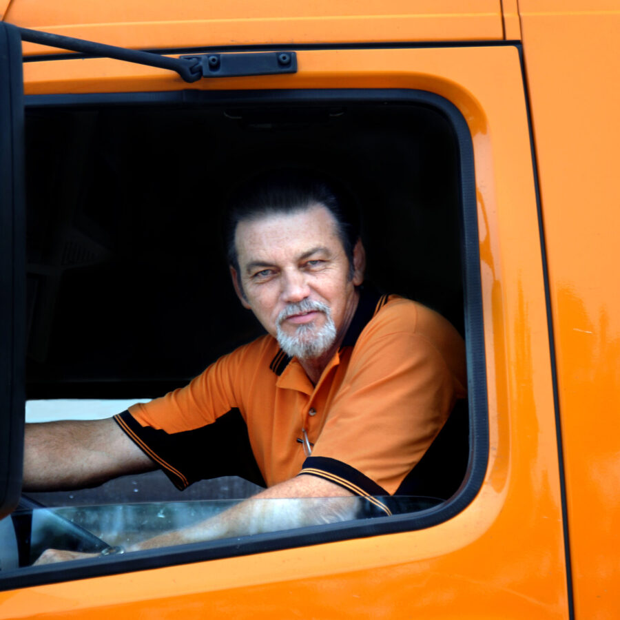 Truck,Driver,Sits,In,Cab,Of,His,Orange,Diesel,Truck.