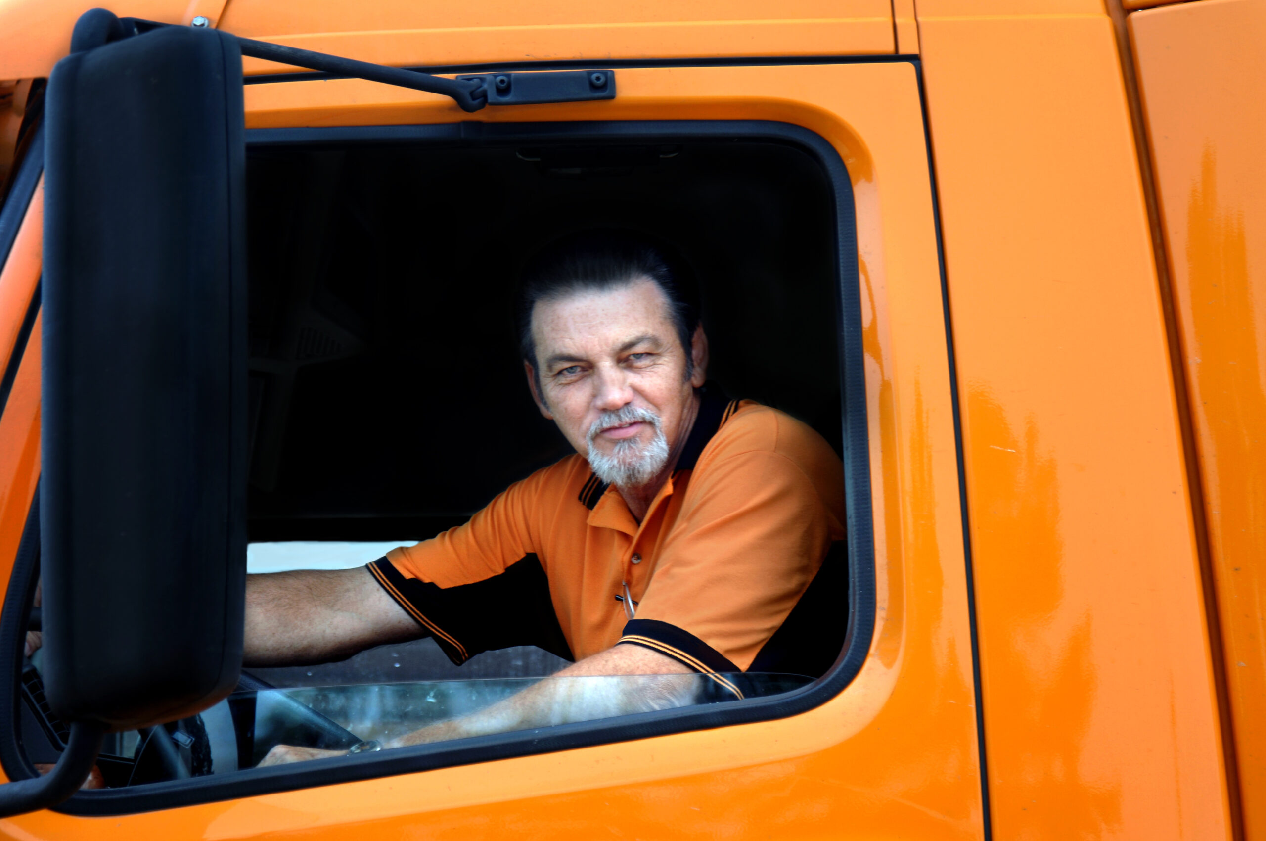 A man in an orange truck looking out the window.